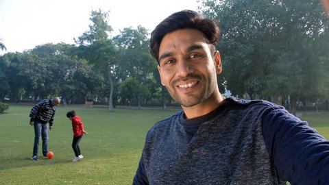 A smiling young man waving his hand and recording a video - picnic, family time, modern-day parenting. An old man and his adorable grandson football in a park - leisure activity, an outdoor sport.