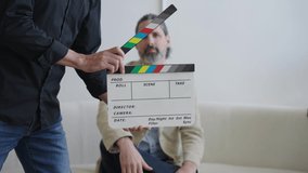 Director Uses Slate On Video Production Film Set in Front of Caucasian Male Actor Dressed in Suit. Camera Changes Focus Between Clapper board and Talent