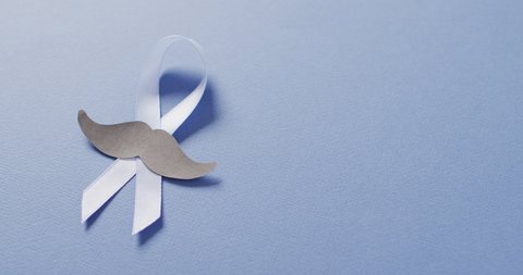 Video of paper moustache and pale blue prostate cancer ribbon on pale blue background. medical and healthcare awareness support campaign symbol for prostate cancer.