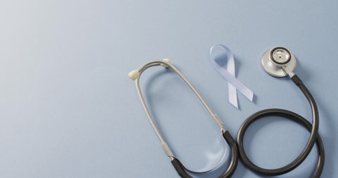 Video of stethoscope and pale blue prostate cancer ribbon on pale blue background. medical and healthcare awareness support campaign symbol for prostate cancer.