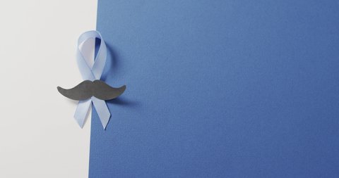 Video of paper moustache and pale blue prostate cancer ribbon on white and blue background. medical and healthcare awareness support campaign symbol for prostate cancer.