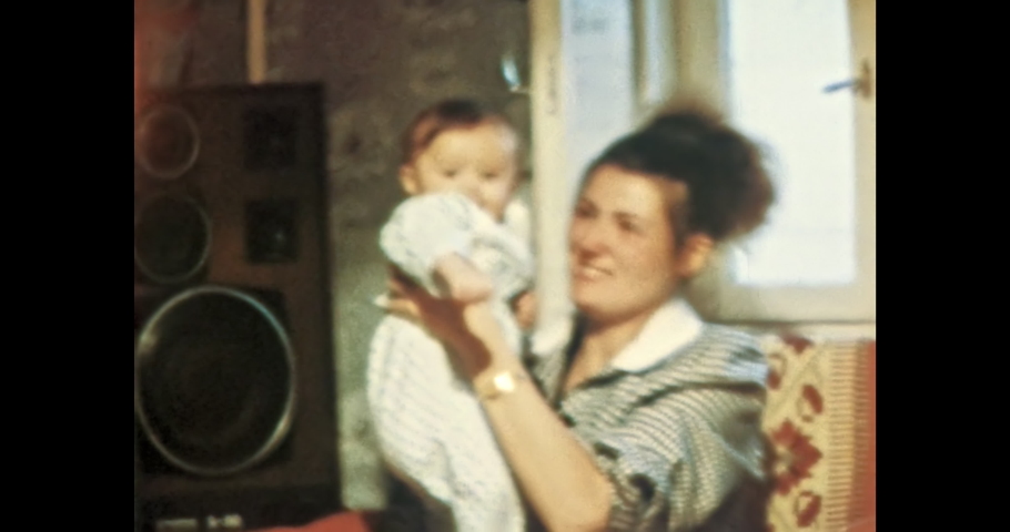 Happy young mother playing with her child at home apartment. Smiling baby with mom in room. Woman's love for child. Vintage color film. Cinema lens flare. Retro 80s, 90s, family archive 8mm