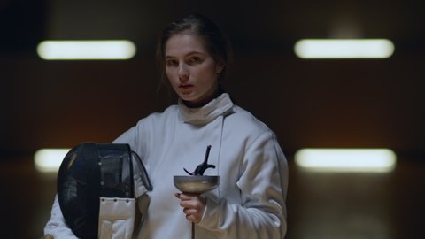 Portrait of female fencer taking off her helmet, posing and looking into camera