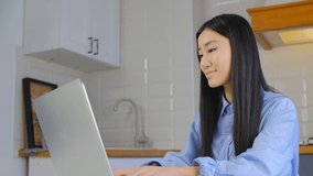 Young asian girl typing text on notebook computer. Cheerful Vietnamese female working on laptop at home. Freelance copy writer woman doing distant work online. BIPOC person lifestyle video clip
