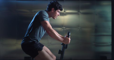 Cinematic shot of young fit virtual instructor or online personal trainer is showing web training workouts plan by using gym cycle in sports studio isolated on background with copy space.