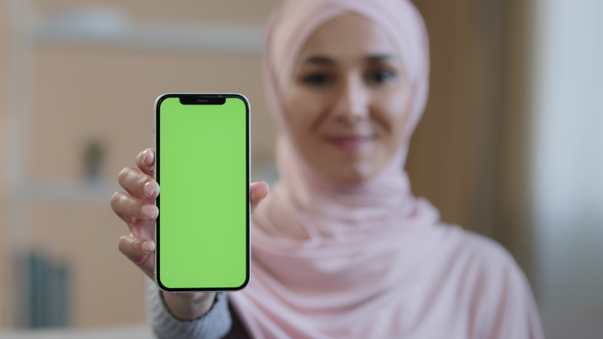 Portrait smiling arabian lebanese girl muslim islamic woman in hijab hold smartphone in front show mobile phone with green screen at camera advertise app service website digital device advertisement Royalty-Free Stock Footage #1090148779