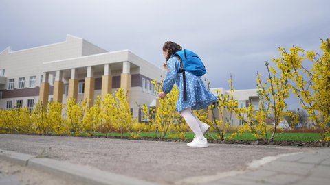 Child in uniform with backpack with textbooks. Girl run from kindergarten to school. Schoolgirl goes to school with smile and fun. Happy joyful girl run to lesson at school.Little child with backpack