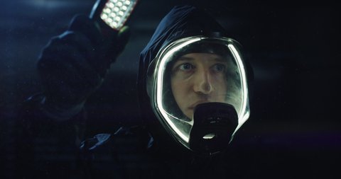 Cinematic shot of futuristic researcher or astronaut wearing led oxygen mask is examining with flashlight mysterious unknown objects or paranormal phenomena in dark suspense.