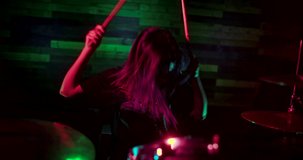 Young beautiful girl playing drums on the stage of nightclub. Light show during the concert. The light flickers to the beat of the drums. Camera moves away from girl drummer