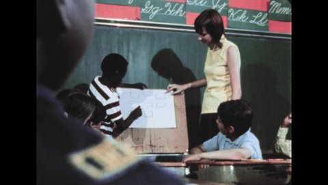 1970s: Child draws line on paper. Children sit at desk, listen. Teacher stands at front of room, watches child draw line on paper. Children play in school yard. Children enter school.
