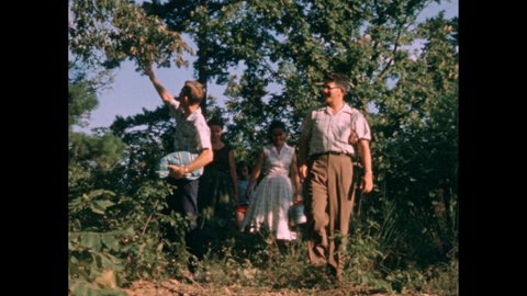 1950s: Child holding clapperboard. People walking through forest, turning, pointing at sky. Children holding basket. Woman holding container.