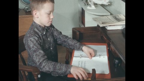 1960s: Boy sitting at desk, reading papers in notebook. Hands holding clapperboard. Boy looking up, down. Child blinking. Woman standing at chalkboard.