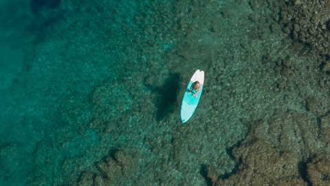Directly above drone shot: Man paddling on a stand up board on turquoise water. People on vacation in Croatia enjoying water sport 