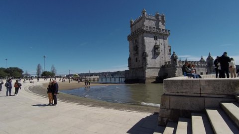 LISBOA, PORTUGAL - Apr 03, 2022: A scenic view of the Belem Tower in Lisbon with tourists walking by under the blue sky