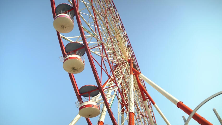 Ferris wheel is close-up, in detail, against blue sky on sunny day side view. booths are full up without people. Slowly. Baumi, Georgia. amusement park. Retro, old image.