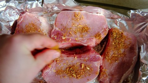 Raw meat steaks on foil. Pork meat sprinkled with spices. Cooking without oil. Preparation for cooking in the oven.