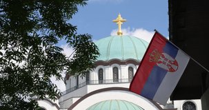 the temple of Saint Sava in Belgrade with a golden cross and the Serbian flag