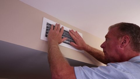 From the left side a homeowner moves both hands in front of a air duct vent to feel for air circulation. Man feeling for air circulation from an air duct outflow vent on a wall near a ceiling