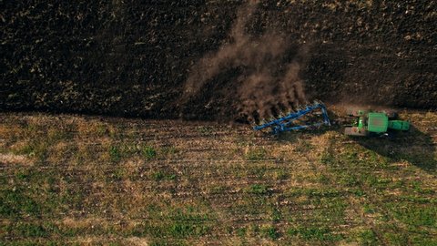 Farm tractor Plowing a field. Tractor with harrows prepares the agricultural land for planting crop in sunset light. Agriculture industry, cultivation of land. Concept: production food, Agriculture.