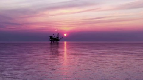 The silhouette of an offshore oil platform in the ocean in front of a beautiful red sky sunset.