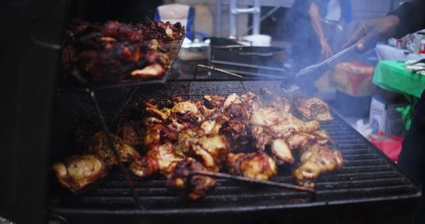 New York, New York United States - May 5, 2022: Close up of man grilling Jamaican Jerk Chicken over Charcoal in city street food festival. Lots of smoke and texture.