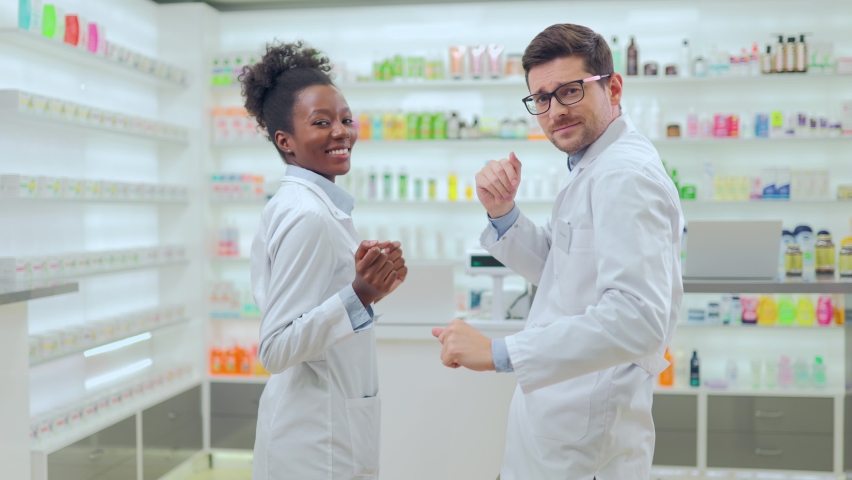 Cheerful african american woman and caucasian man in white lab coats dancing and smiling at modern bright pharmacy. Two pharmacists having fun between clients at work. Royalty-Free Stock Footage #1090170461
