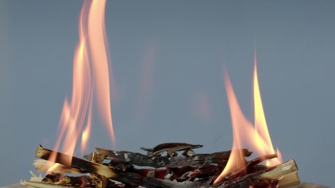 The wooden fire is orange, and the smoke of the fire from the mustard tree is on a grey background. Close-up of a flame with white smoke. Slow motion, 4K.