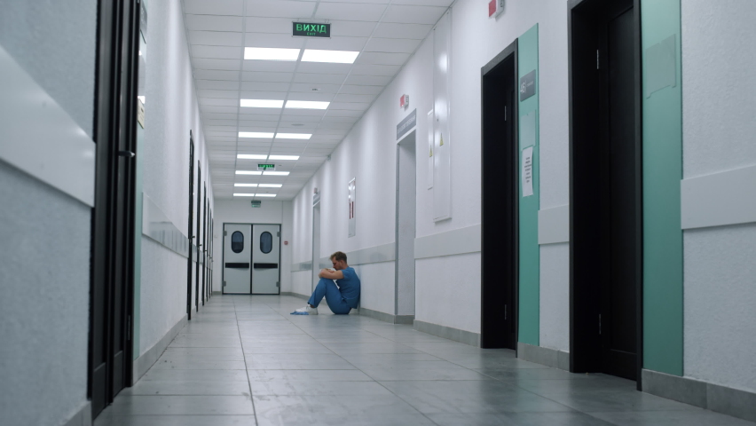 Depressed overwhelmed medicine worker sitting floor long ambulance hallway. Alone stressed man doctor resting hospital corridor. Overworked tired unknown medic professional relaxing after surgery | Shutterstock HD Video #1090170985