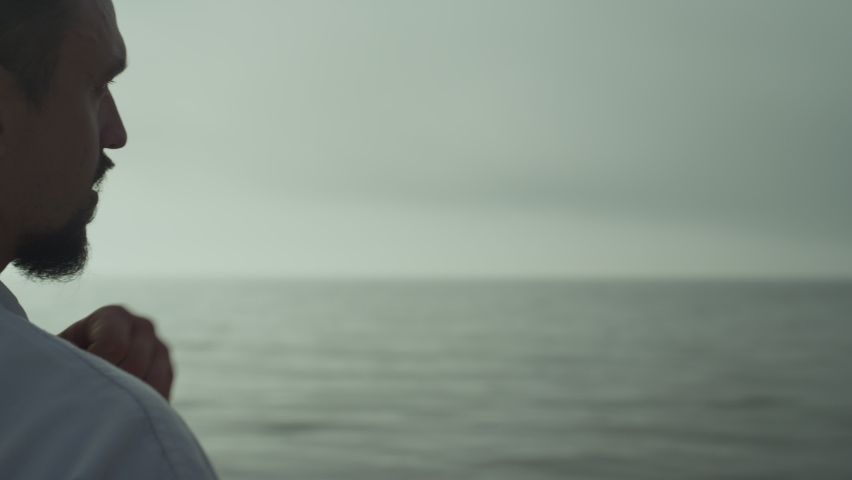 Focused athlete practicing powerful karate punches at sunset outdoor close up. Bearded middle age sportsman making fighting attack wearing kimono near sea waves. Strong man training martial arts.