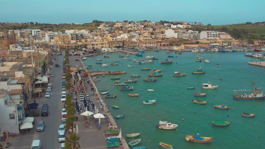 Aerial 4K panoramic footage of Marsaxlokk - small, traditional fishing village in the South Eastern Region of Malta with many colorful fisherman boats in the bay