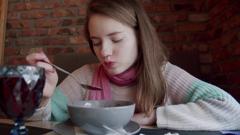 A young girl sits at a table in a cafe and eats borscht. Traditional Ukrainian food