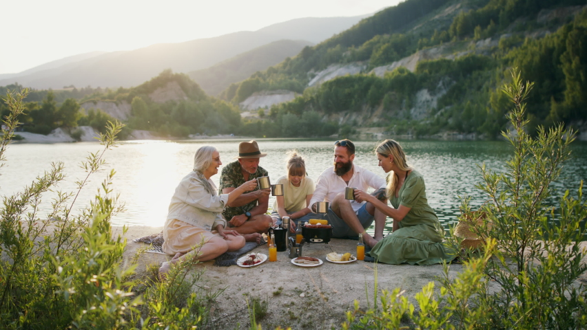 Happy multigeneration family on summer holiday trip, barbecue by lake.