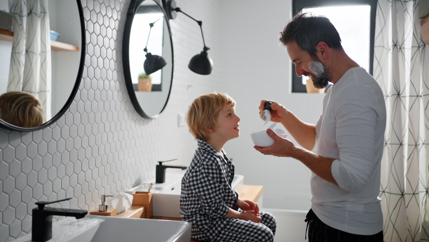 Father with small child indoors in bathroom in the morning at home, shaving. Royalty-Free Stock Footage #1090175949