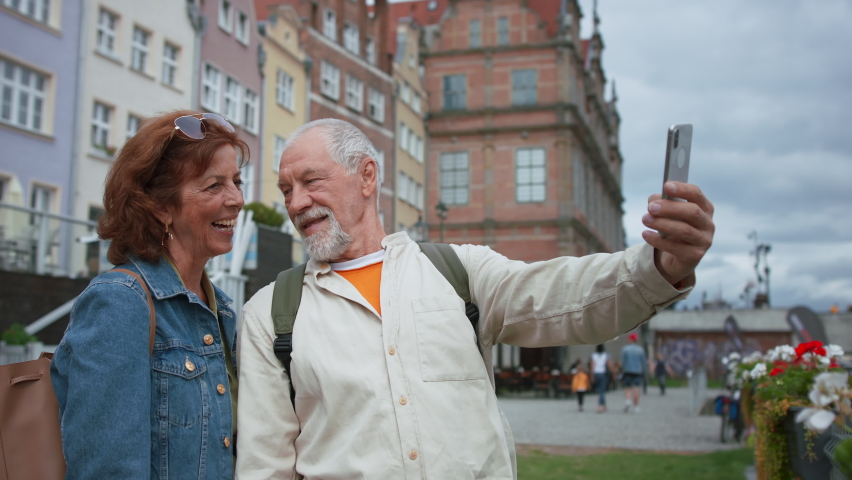 Happy senior couple tourists taking selfie outdoors in historic town