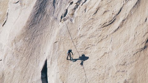 Girl climbs down side of EL Capitan mountain. Rock climbing outside in summer. Woman Hiking Climbing Mountain. Female Climbing by Yosemite Mountains During Summer Vacation Travel Hiking Climbing RED