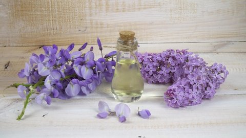 Natural perfume in nice glass bottle on wooden background with purple flowers lilac and wisteria.