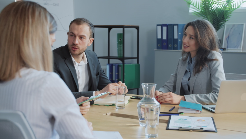 Footage of four Caucasian people sitting at negotiating table, talking. End of business meeting. Man and woman in stylish suits shaking hands and smiling. New business relationships. Good mood. Office Royalty-Free Stock Footage #1090177839