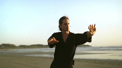 millennial young fit man practice Qi Gong, Tai Chi yoga on beach, summer. outdoor activities, social distancing.