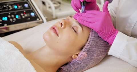 Beautician makes skin care procedure on a  face. Woman in a spa salon on cosmetic procedures for facial care. Cosmetologist making a woman a therapeutic laser processing on a face.
