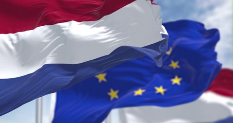 Seamless loop of the national flag of the Netherlands waving in the wind with blurred european union flag in the background on a clear day. Democracy and politics. European country. Selective focus.