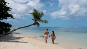 Anse Takamaka beach Mahe Seychelles, is a tropical beach with palm trees and a blue ocean. Seychelles, a couple man and women on the beach walking under a hanging palm tree