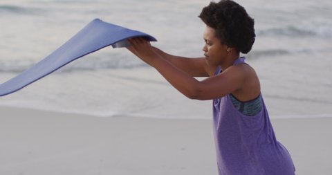 African american woman with yoga mat on sunny beach. healthy and active time beach holiday.