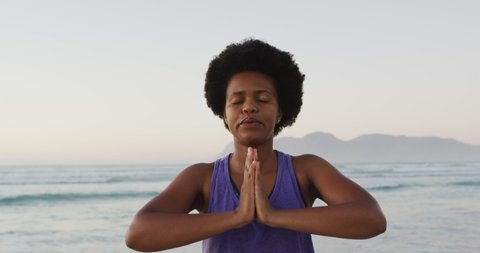 African american woman practicing yoga and meditating on sunny beach. healthy and active time beach holiday.