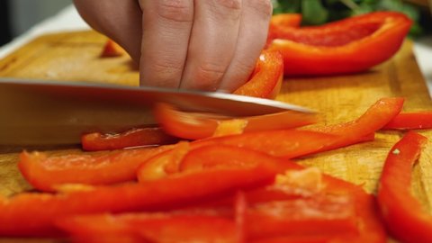 A close-up of a cook slicing red bell peppers with a sharp knife on a kitchen board. Vegetarian Cuisine. The concept of delicious and healthy food. Selective focus