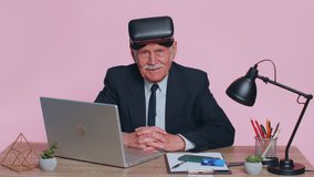 Senior businessman using headset helmet app to play simulation game. Watching virtual reality 3D 360 infographic video at office. Elderly man in VR goggles isolated indoor on pink studio background