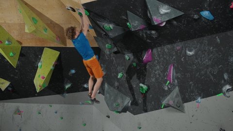 Slow motion, young man professional climber training on a climbing wall, practicing rock-climbing and moving up, self-improvement.