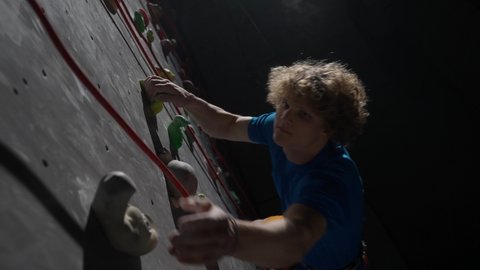 Young man professional climber training on a climbing wall, practicing rock-climbing and moving up, using insurance, cinematic lighting.
