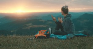 Woman hiker, hiking backpacker traveler camper with her phone camera on the top of mountain in sunny day under sun light. Beautiful mountain landscape view. Hiking, backpacking. 4K slow motion video