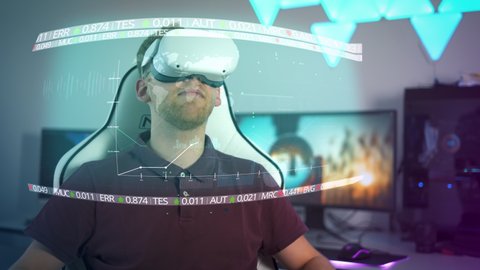 Young man with VR AR glasses sitting in study looking at futuristic virtual reality technology stock analysis and digital chart financial market prices