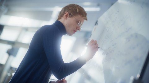Young Male Scientist Smiling, Find Solutions and Write Formulas at the Whiteboard. Education, Learning and Startup Concept. Low Angle View